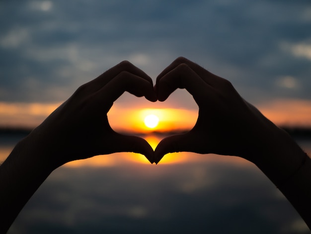 Silhouette hands to be heart shape on sunset background. 