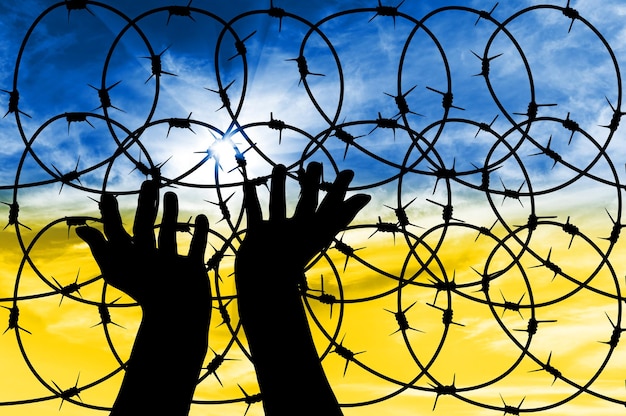 Silhouette of hands facing the sky against the background of a fence with barbed wire Concept of war and crisis in Ukraine with Russia