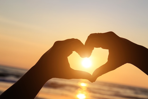 Silhouette of hands in heart  symbol around the sun