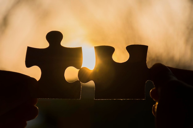 Silhouette hands holding jigsaw pieces against sky during sunset