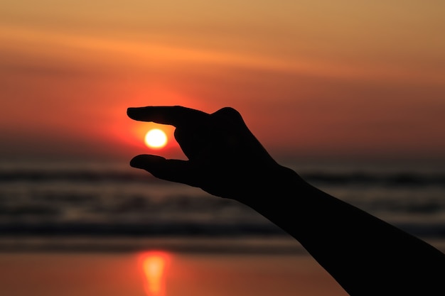 Silhouette of hands play with the sun at neach in sunset time