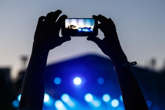 Siluetta delle mani che scattano una foto con il telefono cellulare su un concerto con la luce del palcoscenico