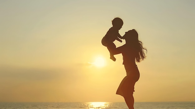 Silhouette of happy Asian mother holding her kid at the beach during sunset