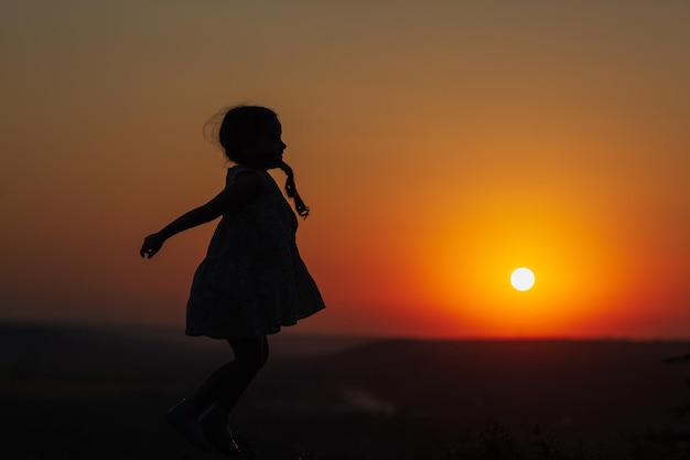 夕日にジャンプする幸せな子供のシルエット