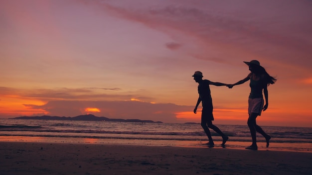 Силуэт счастливой любящей пары встречается и играет на пляже на закате на берегу океана