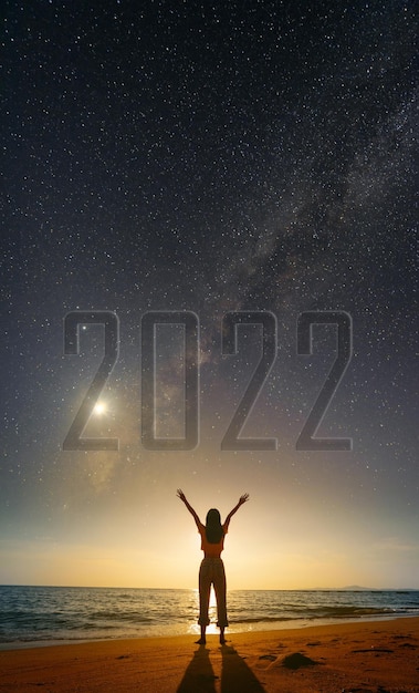 Silhouette of happy woman standing on the beach under starry\
night sky with milky way with text 2022