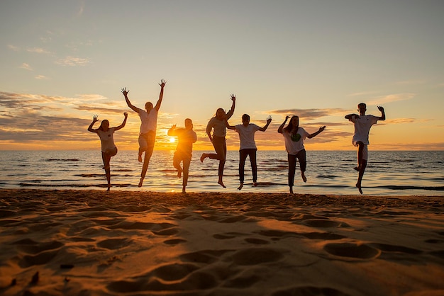 Silhouette of happy young people at sunset by the sea jumping and playing volleyball ball