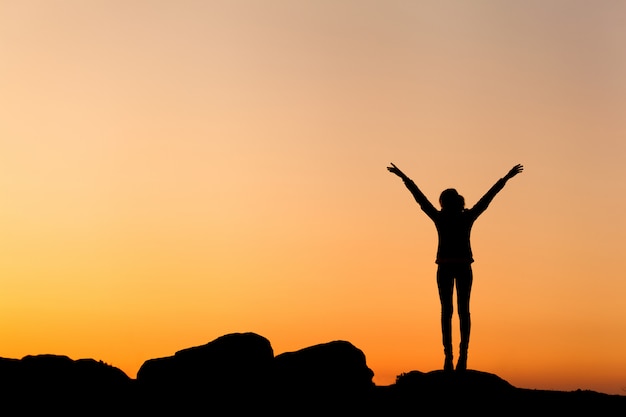 Silhouette of happy young woman against beautiful colorful sky