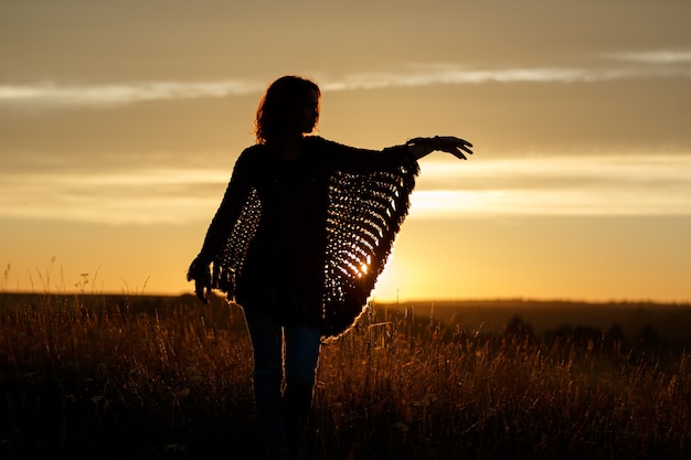 Silhouette of happy young woman on sunset , outdoor girl in a plaid poncho in a field with spikelets