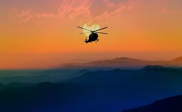 silhouette helicopter flying over mountains against sky during sunset