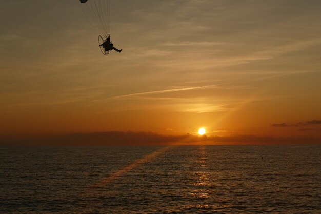 Silhouette of helicopter in sea against sky during sunset