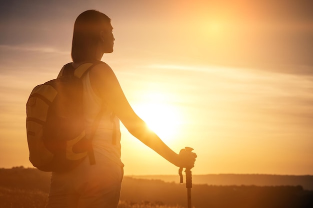 Silhouette donna escursionista inseguimento con zaino e palo da trekking tramonto cielo arancione sullo sfondo