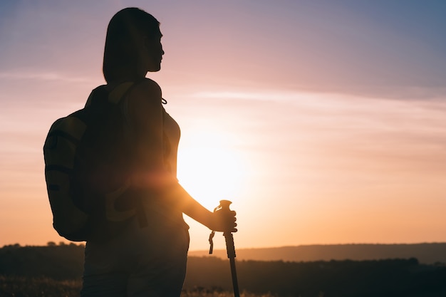 Silhouette hiker woman tracking with backpack and trekking pole, sunset orange sky on the