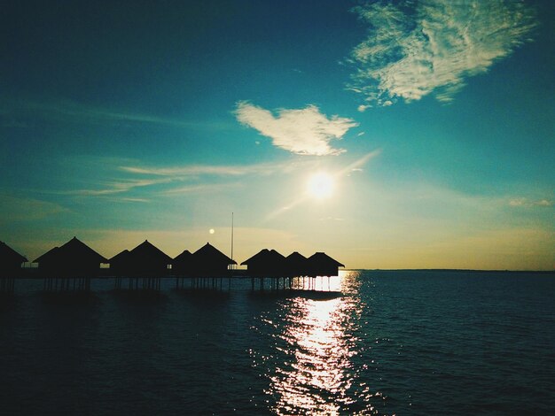 Silhouette houses by sea against sky during sunset