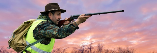 Силуэт охотника на фоне утренней красной зари Стоит наготове с ружьем