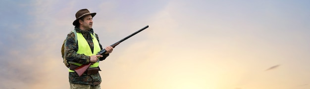 Silhouette of a hunter on the background of the morning red dawn. Stands at the ready with a gun.