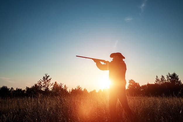 美しい夕日に彼の手で銃を持つカウボーイハットでハンターのシルエット