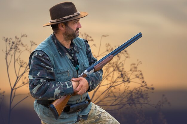 Photo silhouette of a hunter with a gun in the reeds against the sun, an ambush for ducks with dogs