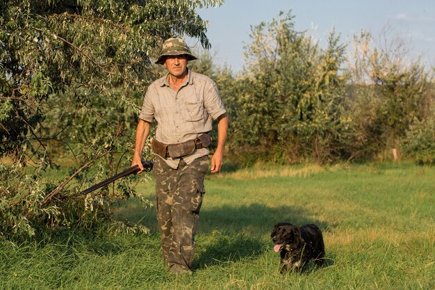 太陽に対して葦に銃を持ったハンターのシルエット、犬とアヒルの待ち伏せ