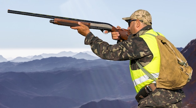 Silhouette of a hunter with a gun in the reeds against the sun, an ambush for ducks with dogs