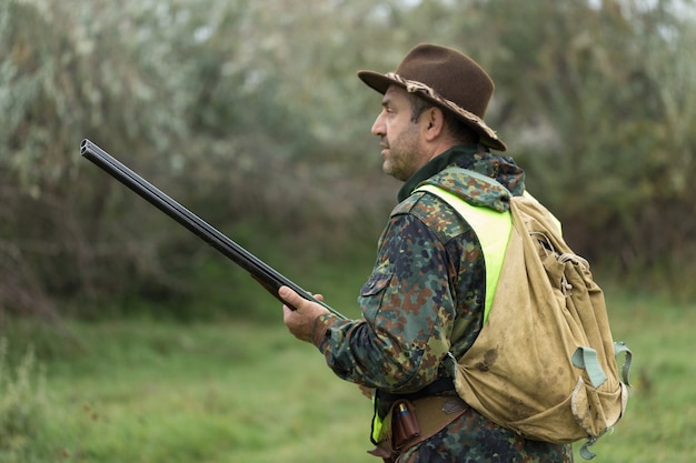 Silhouette of a hunter with a gun in the reeds against the sun, an ambush for ducks with dogs