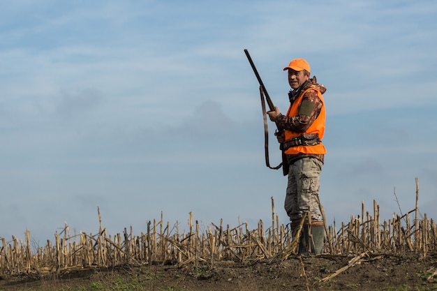 Silhouette of a hunter with a gun in the reeds against the sun, an ambush for ducks with dogs