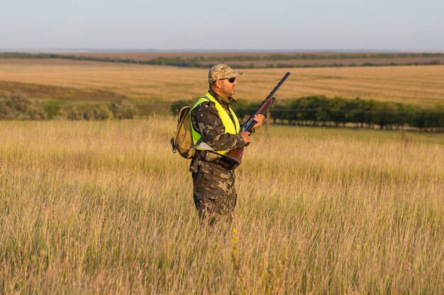 Silhouette of a hunter with a gun in the reeds against the sun an ambush for ducks with dogs