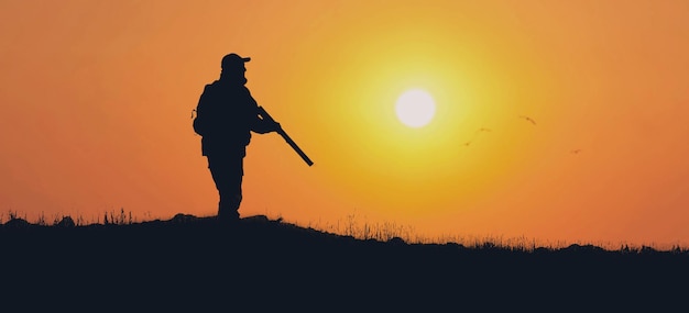 Silhouette of a hunter with a gun in the reeds against the sun an ambush for ducks with dogs