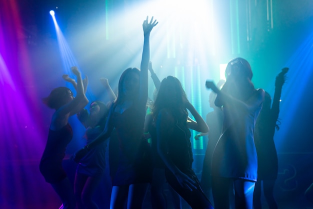 Silhouette image of people dance in disco night club to music from DJ on stage