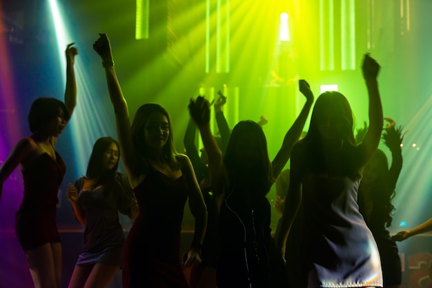 Silhouette image of people dance in disco night club to music from DJ on stage