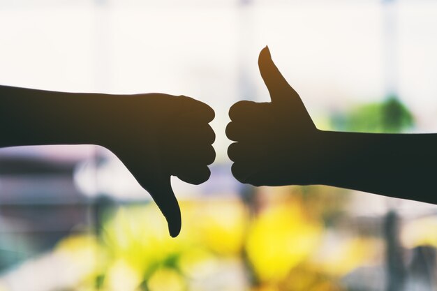 Silhouette image of two hands making thumbs up and thumbs down sign