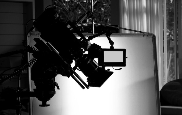 Silhouette images of video camera in tv commercial studio production which operating or shooting by cameraman and film crew team in set and prop on professional crane and tripod for easy to use