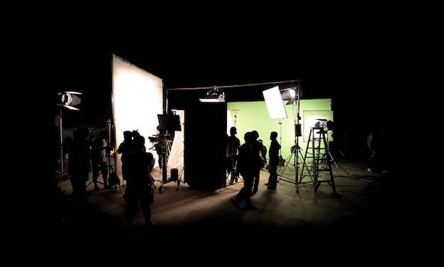 Silhouette images of video production behind the scenes or b-roll or making of TV commercial movie that film crew team lightman and cameraman working together with director in studio with equipment