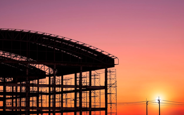 Silhouette of industrial building structure with curved roof in construction site at sunset