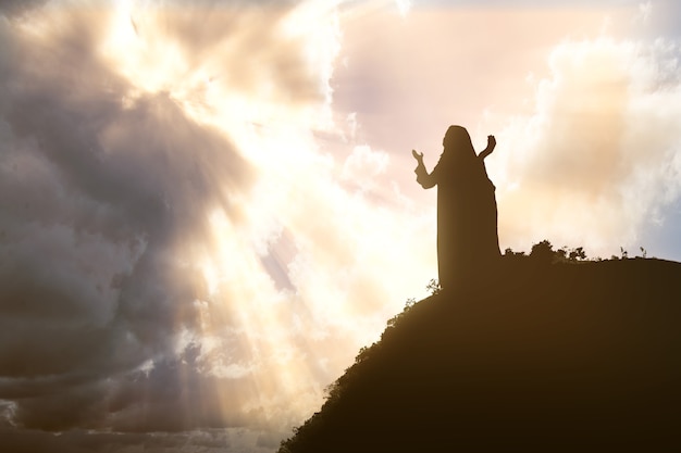 Photo silhouette of jesus christ praying to god with a dramatic sky