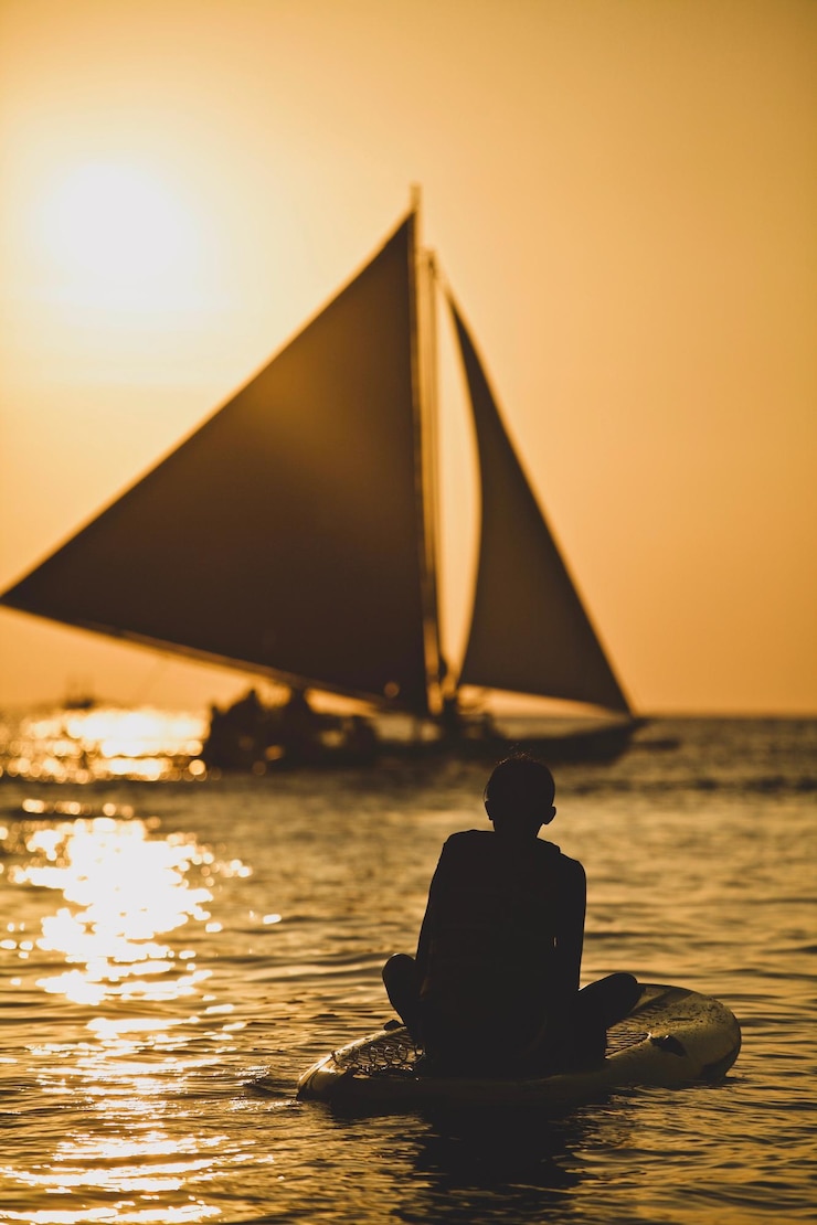 Foto silhouette jongen paddleboarden in de zee tegen de hemel tijdens zonsondergang