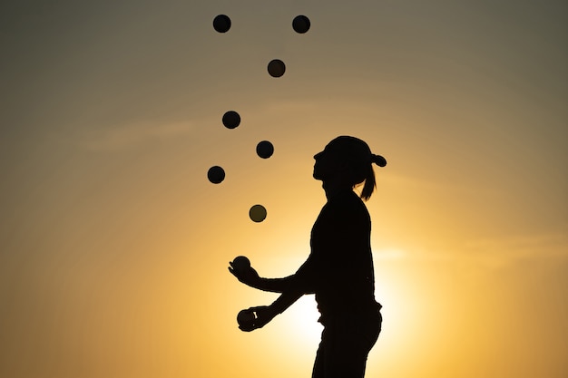 Silhouette of juggler with balls on colorful sunset.