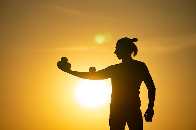 Silhouette of juggler with balls on colorful sunset.