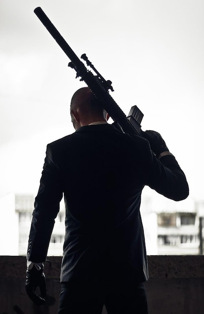 The silhouette of a killer in a suit or killer with weapons per day, holding a sniper rifle.