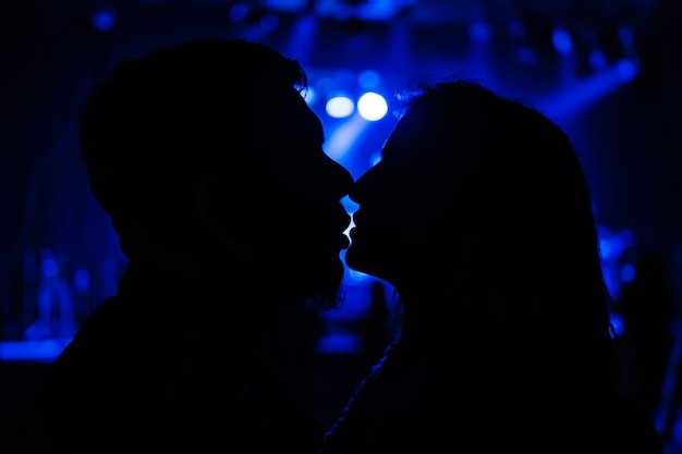 Silhouette of kissing man and woman on blurred background with blue lights