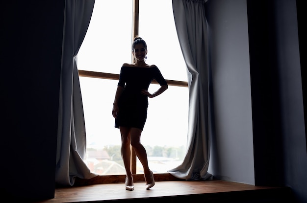 Silhouette of a lady in a short dress near the window curtains\
room model