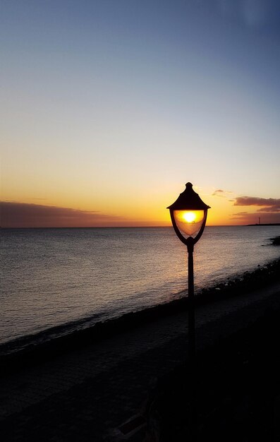 Silhouette lamp by sea against sky during sunset