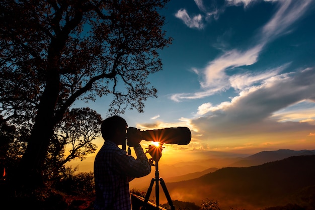 La siluetta di un fotografo di paesaggio usa il teleobiettivo eccellente in cima alle montagne durante il tramonto con il cielo del tramonto di due toni