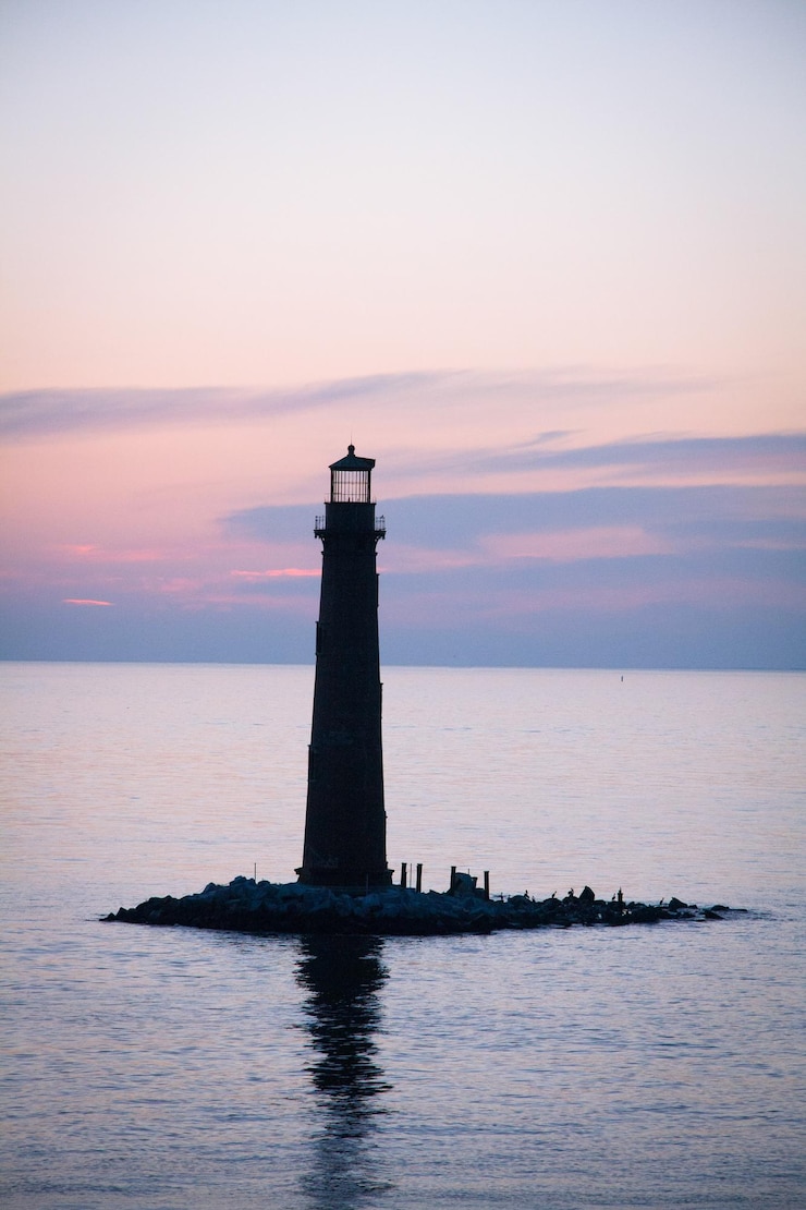 Photo silhouette lighthouse amidst sea against sky at sunset