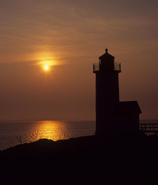 Photo silhouette lighthouse by sea against orange sky