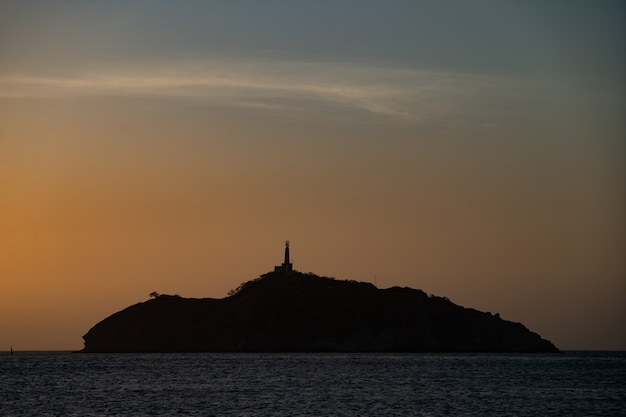 旅行と冒険の海の概念の小さな岩の島の頂上に灯台のシルエット