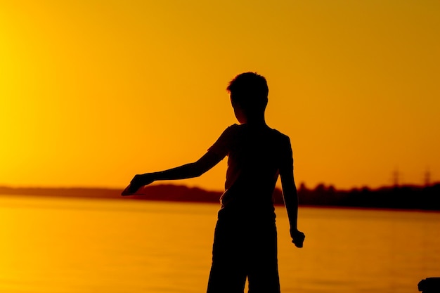 Silhouette of little boy in the sunset landscape in front of evening river Boy at the river sunset background standing and looking ahead