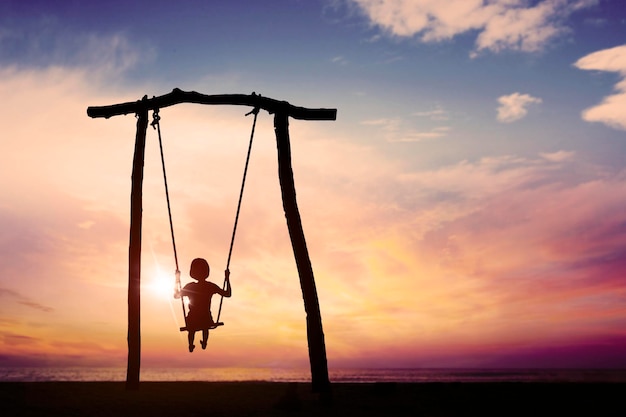 Silhouette of little girl playing with swings on beach