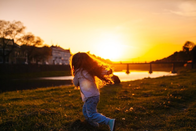 Silhouette of a little girl who runs fast at the river during the sunset