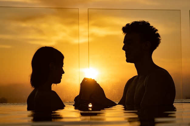 Foto siluetta delle coppie amorose nell'acqua del palo dell'infinito durante il tramonto. romanticismo e relazione